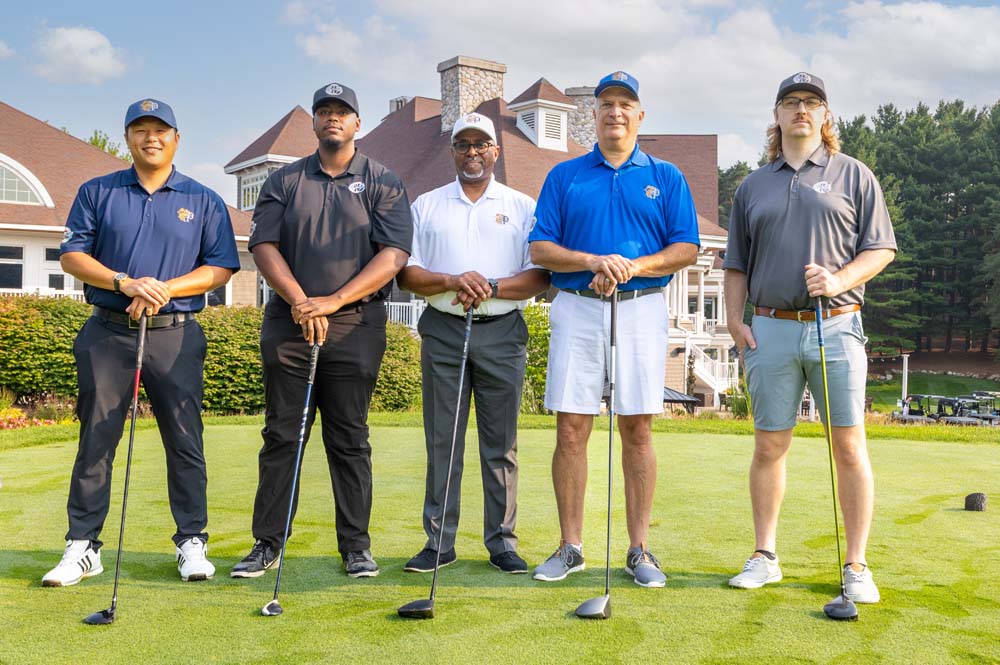 Five men posing with golf clubs on a golf course in Power Collection Clothing
